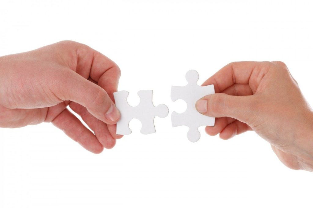 two hands holding a puzzle piece each, attempting to join them together